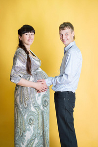 怀孕的黑发女人和丈夫在黄色背景。夫妇