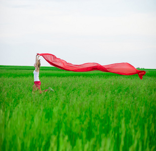 年轻的女士跑与组织在绿色的田野。女人用围巾