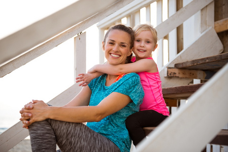 健康的母亲和宝贝女儿拥抱在楼梯上的海边的房子