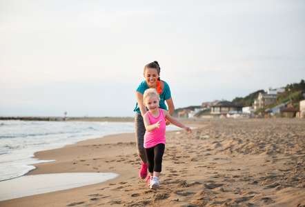 健康的母亲和女婴在海滩上运行