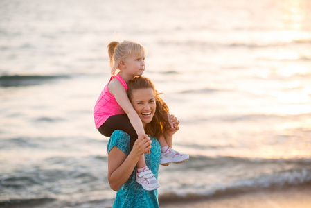 快乐宝贝女孩坐在母亲的肩膀上 e 在海滩上