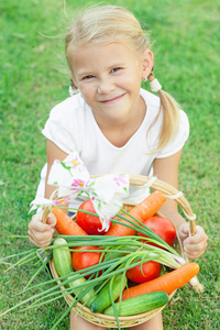 快乐的小女孩坐在草地与一篮子蔬菜上