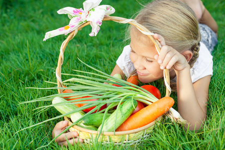 快乐的小女孩躺在草地上放着一个篮子蔬菜