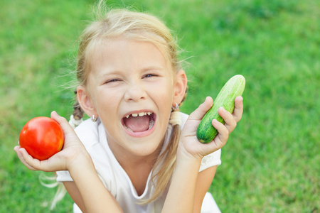 快乐的小女孩坐在与蔬菜在草地上