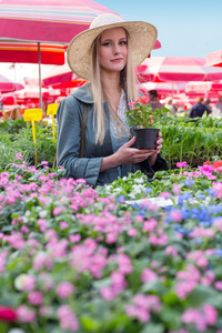 有吸引力的金发女孩，与持有花盆花卉市场上的那顶草帽