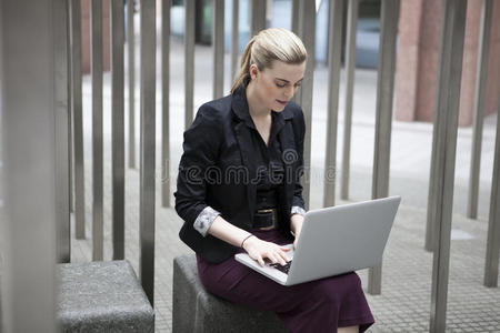 年轻的女商人拿着笔记本电脑坐在外面