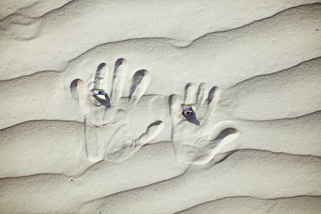 与手印在白色的沙滩上的结婚戒指