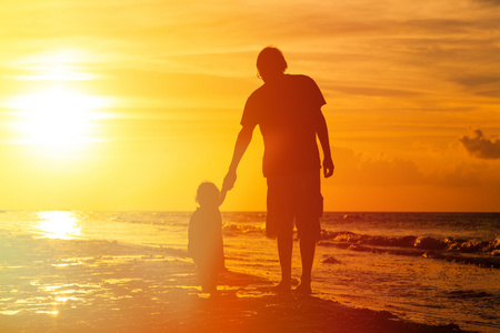 父亲和小女儿散步在日落时的剪影照片