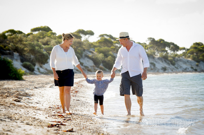 年轻的快乐母亲和父亲在家庭度假概念在沙滩上行走