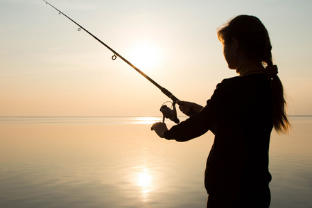一个年轻的姑娘在海边日落钓鱼的剪影