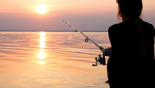 年轻的姑娘在海边日落钓鱼