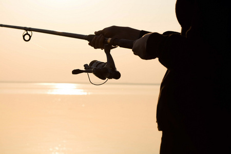 在日落时在海边钓鱼杆渔夫剪影