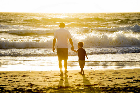 快乐的父亲牵握的小儿子在海滩上，赤脚走在一起