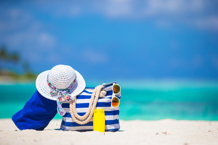 蓝色条纹袋和毛巾，稻草白色帽子，太阳镜，防晒霜瓶在异国风情的沙滩上
