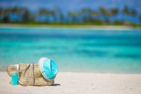 稻草袋，蓝色的帽子，墨镜和防晒霜瓶热带海滩上