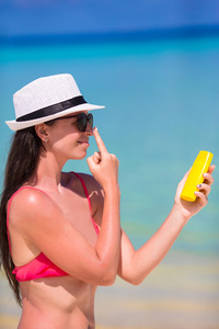年轻快乐的女人，在她鼻子上的白色沙滩上应用防晒霜