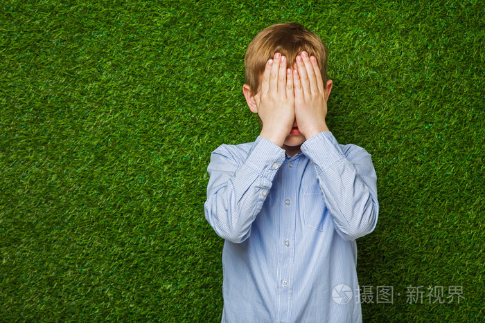 衬衫在绿色的草地隐藏他的眼睛的男孩