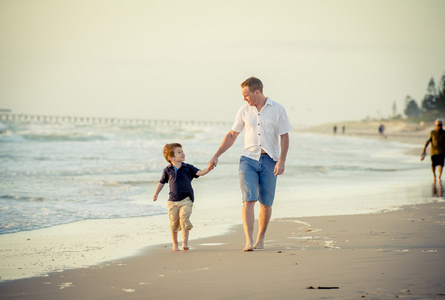 快乐爸爸玩在沙滩上与运行的小儿子兴奋与赤脚在沙子和水