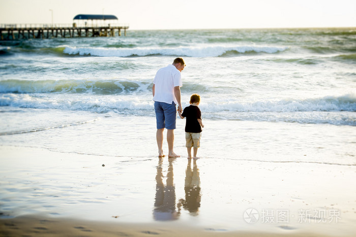 快乐的父亲牵握的小儿子在海滩上,赤脚走在一起