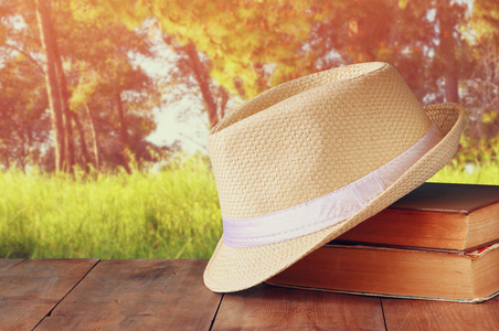头戴呢帽和一摞书在木桌和晚上自然国家侧背景。放松或度假的概念