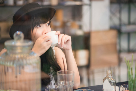 年轻的亚洲女人喝咖啡，透过这面镜子