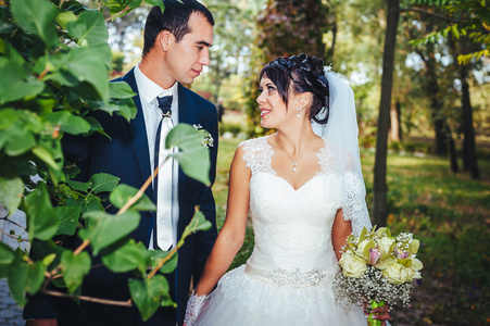 接吻的结婚礼服的年轻夫妇。新娘控股束鲜花