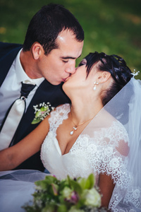 接吻的结婚礼服的年轻夫妇。新娘控股束鲜花