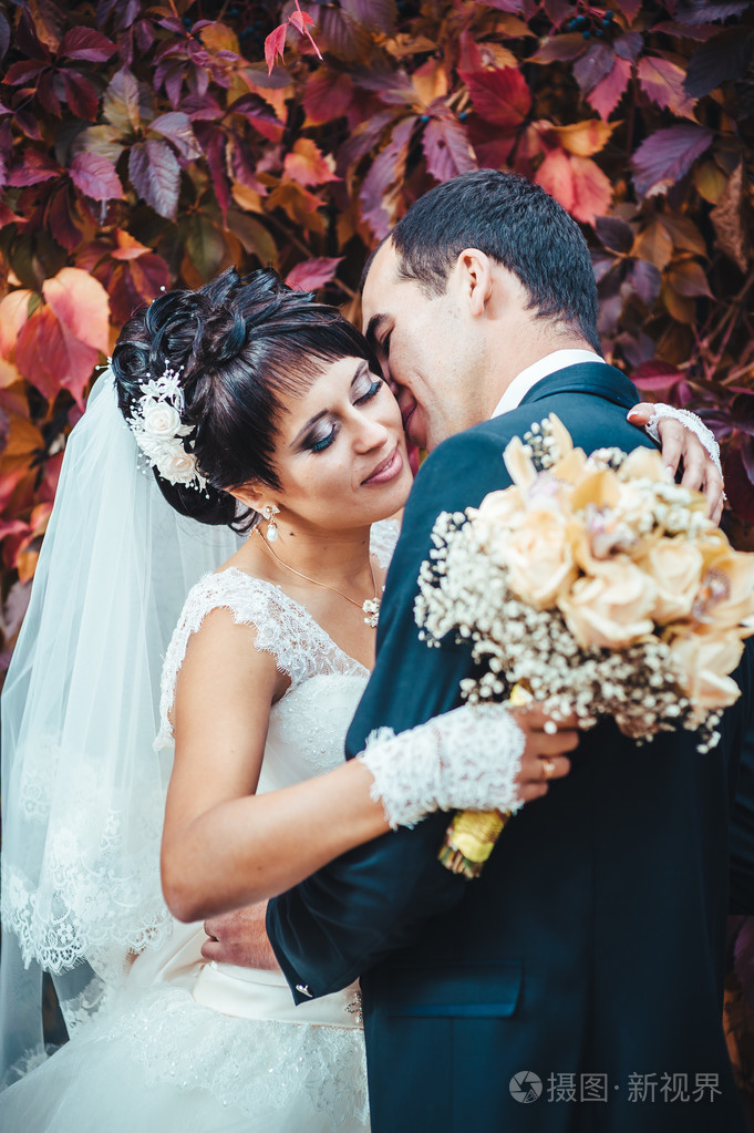 接吻的结婚礼服的年轻夫妇.新娘控股束鲜花