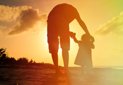 父亲和小女儿在日落时在海滩上行走