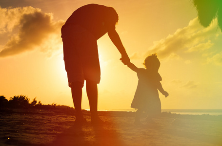 父亲和小女儿在日落时在海滩上行走