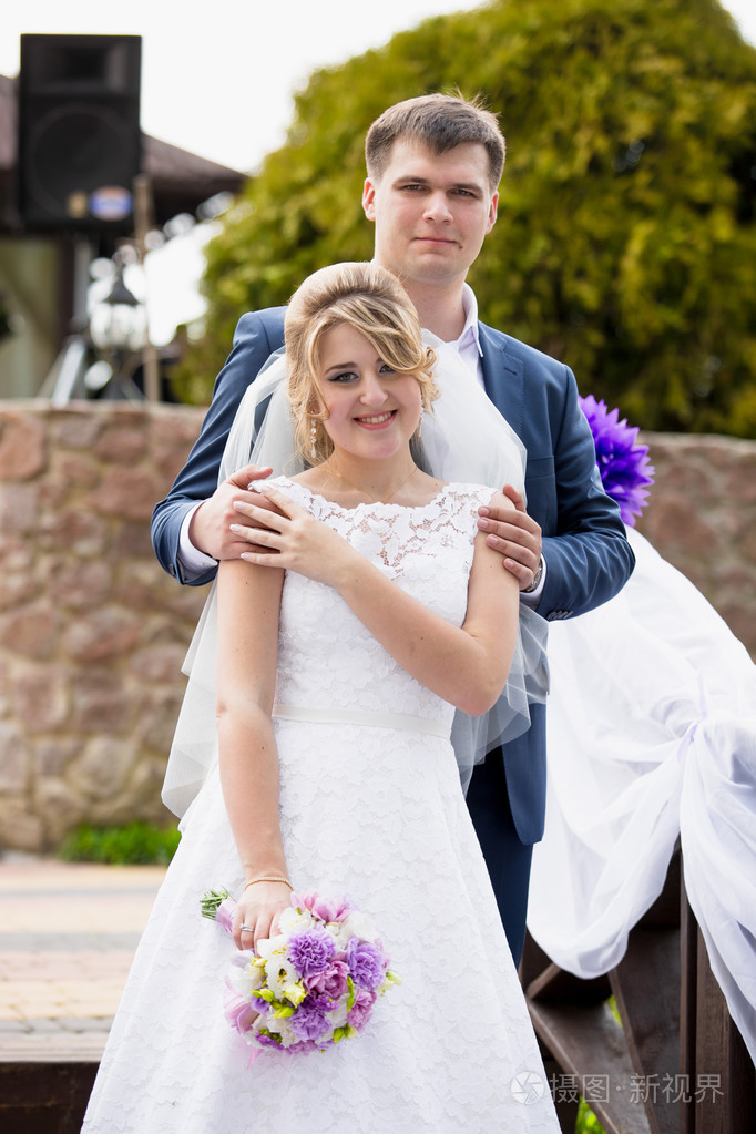 年轻的新郎拥抱可爱新娘在肩上