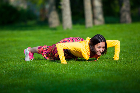 按 ups 锻炼的年轻女子。女孩做草运动量来找到力量训练在早晨的太阳的光芒