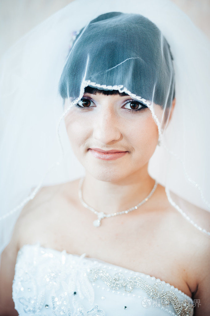美丽的新娘准备在白色的婚纱礼服发型与亮妆快乐的性感女孩等待新郎