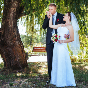 新娘和新郎在婚礼当天到户外散步在春天性质。新婚夫妇，祝新婚快乐女人和男人拥抱绿色的公园里。爱婚礼情侣户外