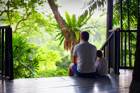 父亲和儿子坐在热带森林中的树上的房子楼梯上