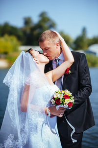 在海边的婚礼。我们的蜜月。新娘和新郎在湖岸的拥抱。新郎和新娘拥抱绿色的湖面上。新郎和新娘在公园里。婚纱礼服。新娘婚礼花束的花朵