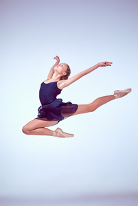 美丽的年轻芭蕾舞演员跳上一个灰色背景