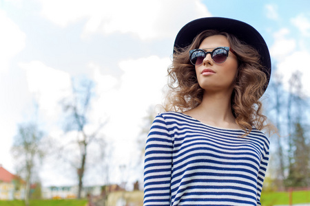 明亮美丽的年轻快乐的女孩在帽子和太阳镜在晴朗的一天在公园散步