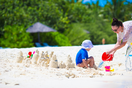 热带度假玩沙滩玩具的小女孩和年轻妈妈