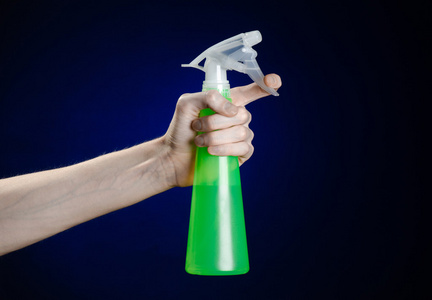 清洁的房子和更清洁的主题 人的手拿着绿色喷雾瓶清洗上的深蓝色背景