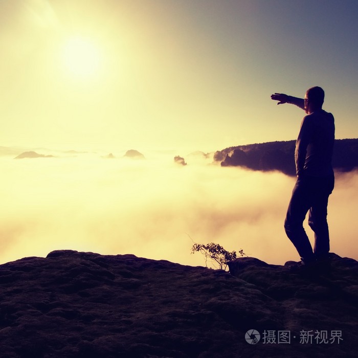 男人穿着衬衫和牛仔裤是站在峰顶的砂岩帝国和注视着朦胧有雾的早晨谷