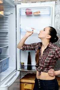 女孩在打开的冰箱旁喝酸奶