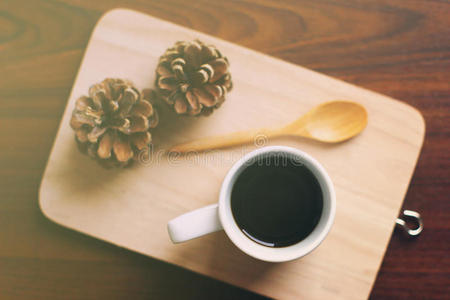 黑咖啡和勺子放在木制托盘上，带有松果，复古过滤效果