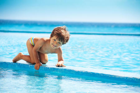 小男孩爬上游泳池的木板