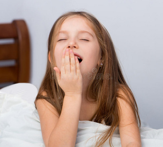 小女孩打哈欠穿着运动服的可爱小女孩的肖像. 她坐着,从疲倦中打哈欠.