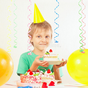 戴着节日帽的小男孩拿着生日蛋糕和气球