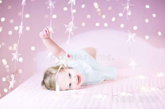 可爱的蹒跚学步的女孩玩她的玩具熊之间的软灯在星星形状