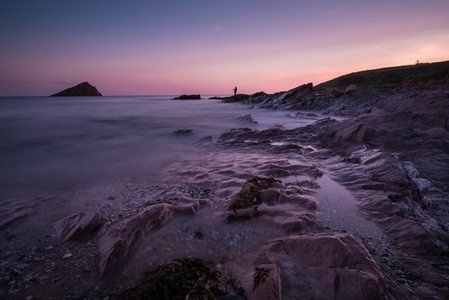 黄昏时宁静的海景，岩石海滩上有渔夫的轮廓