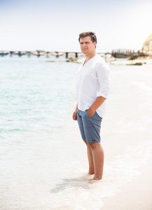 时尚的男人，穿着衬衫和短裤，站在沙滩上