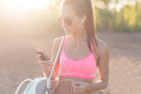 看着智能手机后，锻炼在大自然户外人像夏天晚上在海滩假日和假期健康的生活方式的运动员女人听音乐